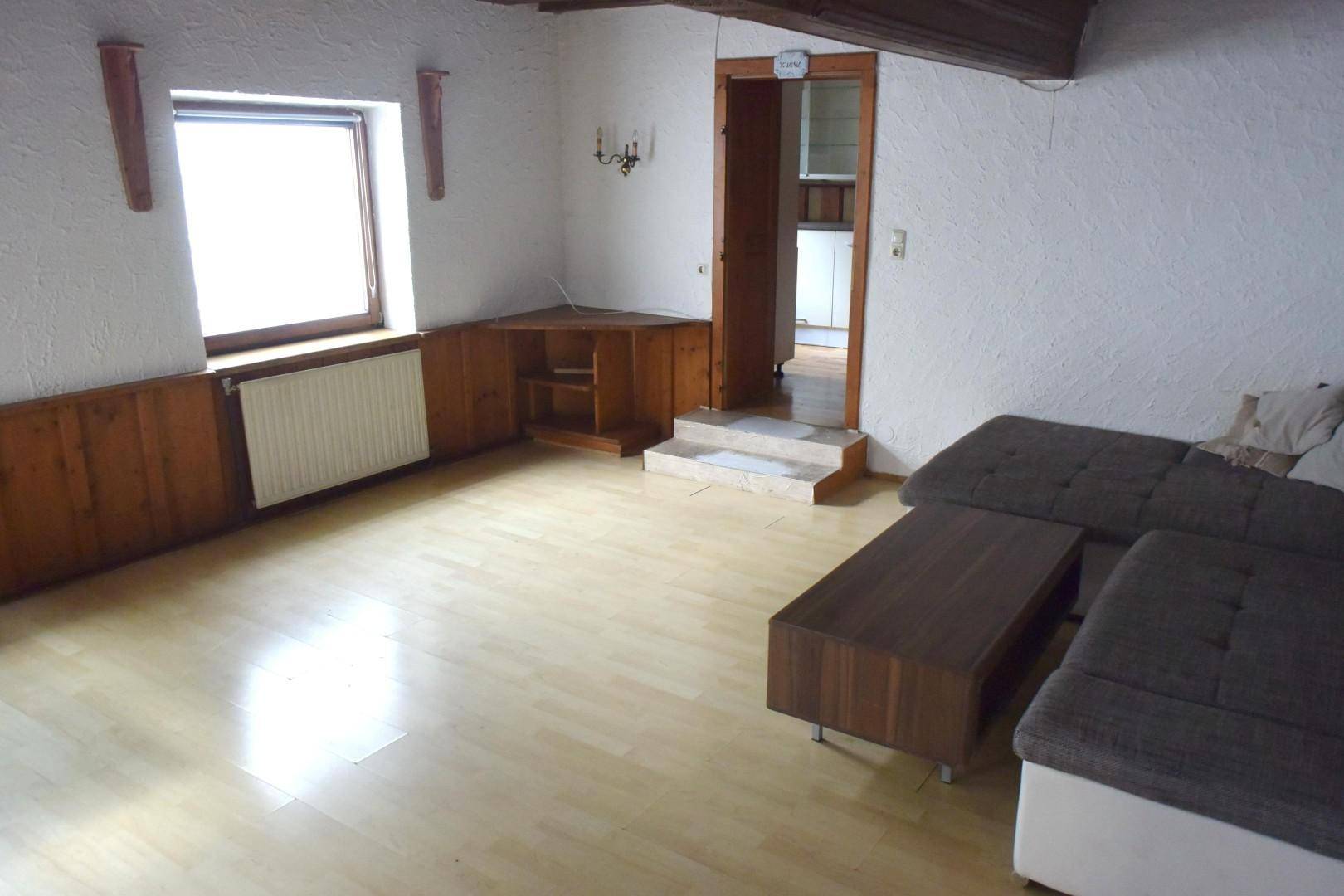 Gemütliches Wohnzimmer mit hellem Holzboden, Sofa und Holzvertäfelung an den unteren Wänden.