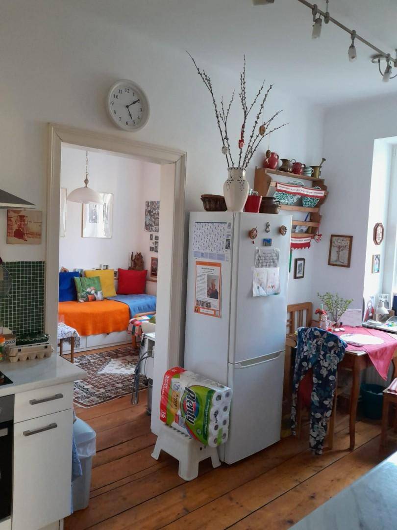 Helle Küche mit Kühlschrank und Essbereich, die einen Blick in ein angrenzendes Zimmer mit Holzboden bietet.