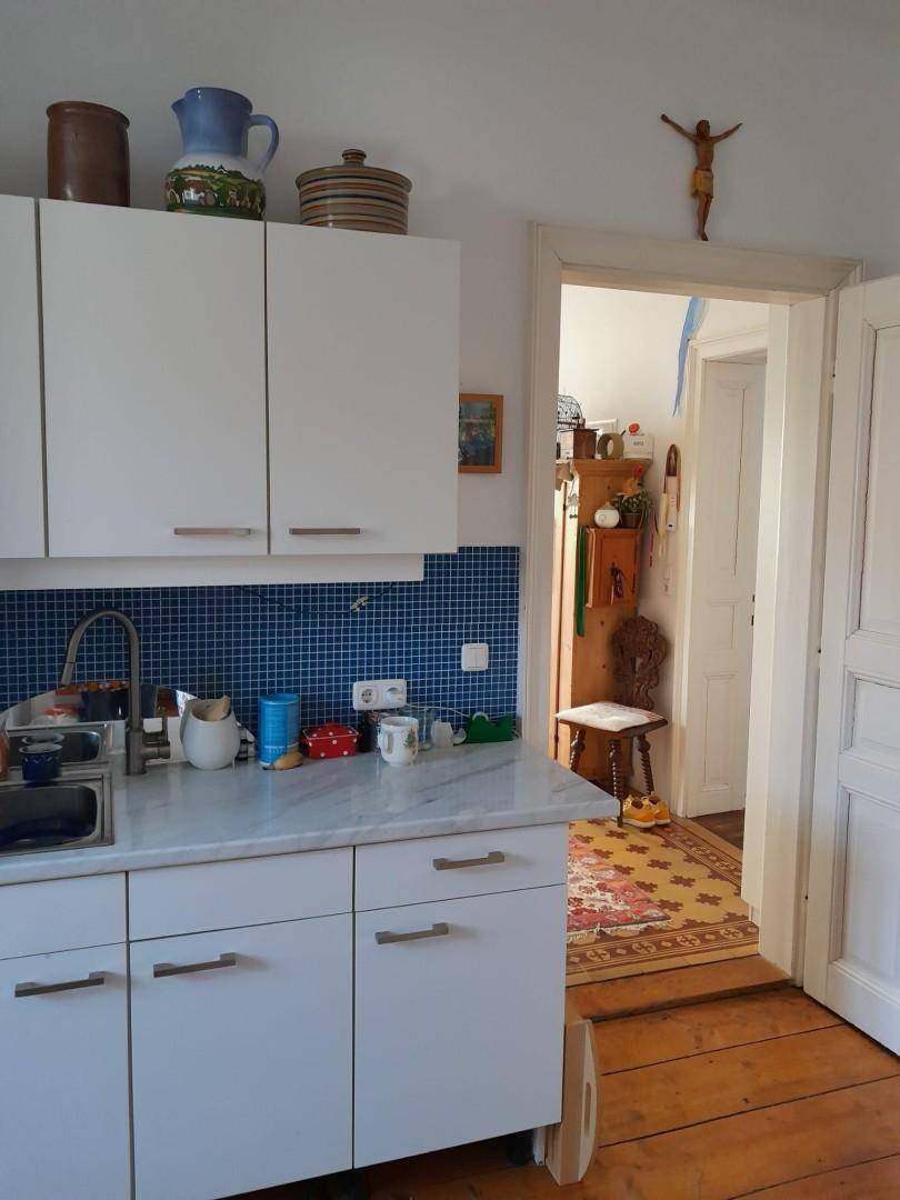 Funktionale Küche mit weißen Schränken, Marmorarbeitsplatte und blauen Mosaikfliesen als Spritzschutz.
