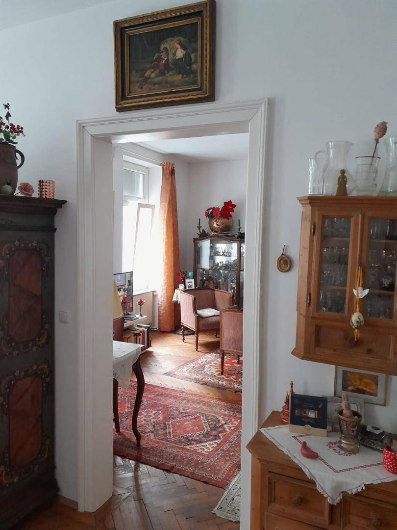 Gemütliches Wohnzimmer mit traditionellen Möbeln, Teppich und warmen Farbakzenten, durch eine Tür sichtbar.