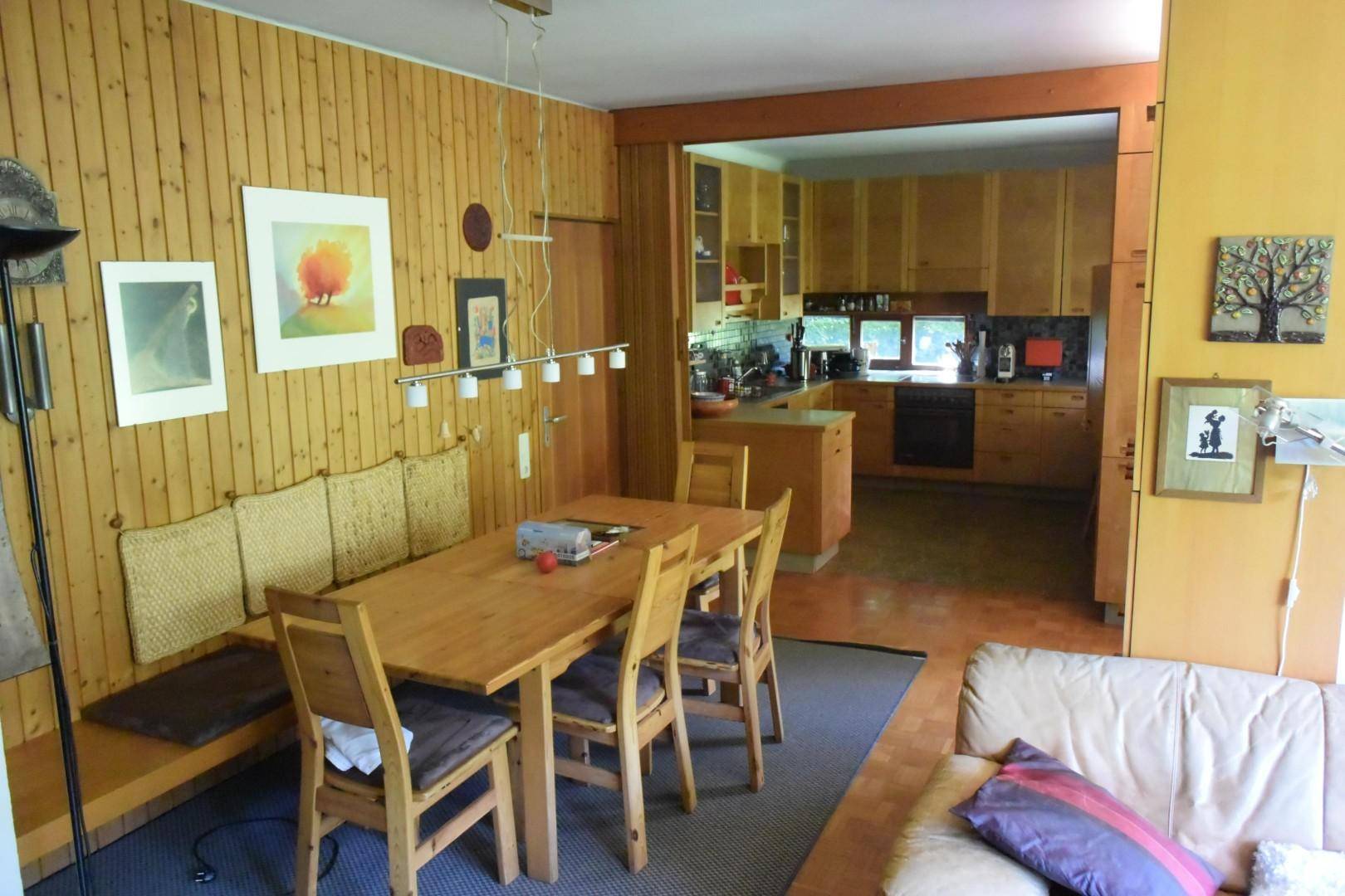 Gemütlicher Wohn-Essbereich mit Holztisch, Sitzbank und offenem Zugang zur Küche.