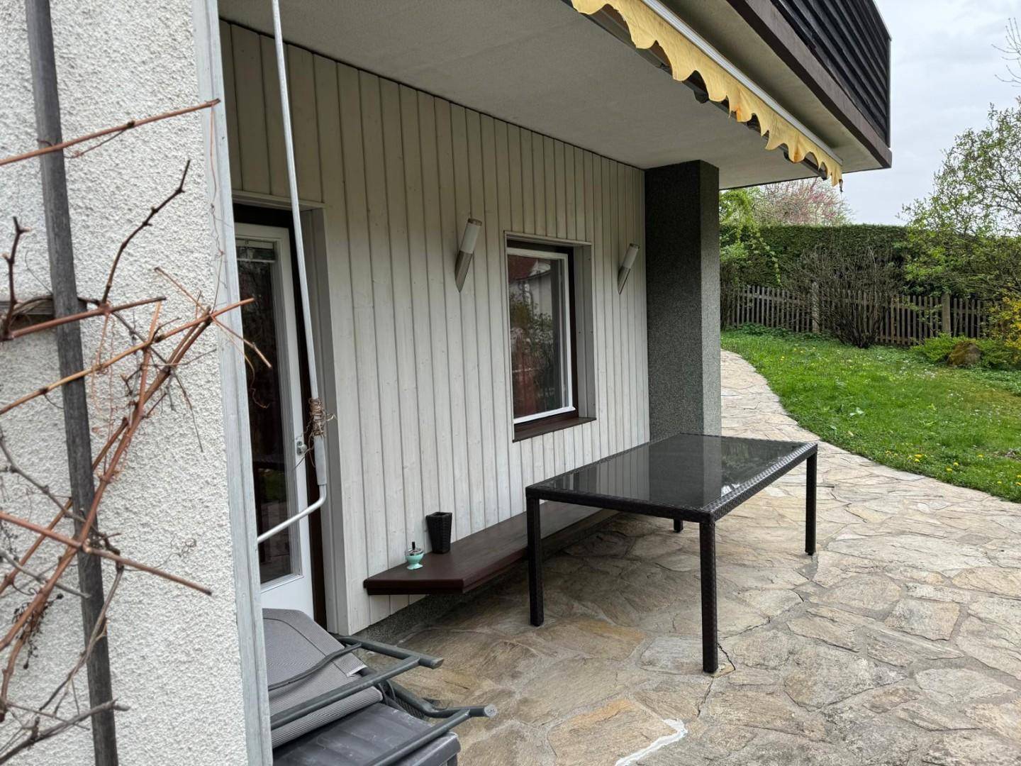 Gepflasterte Terrasse mit einem Tisch und einer Bank, umgeben von einem gepflegten Gartenbereich.