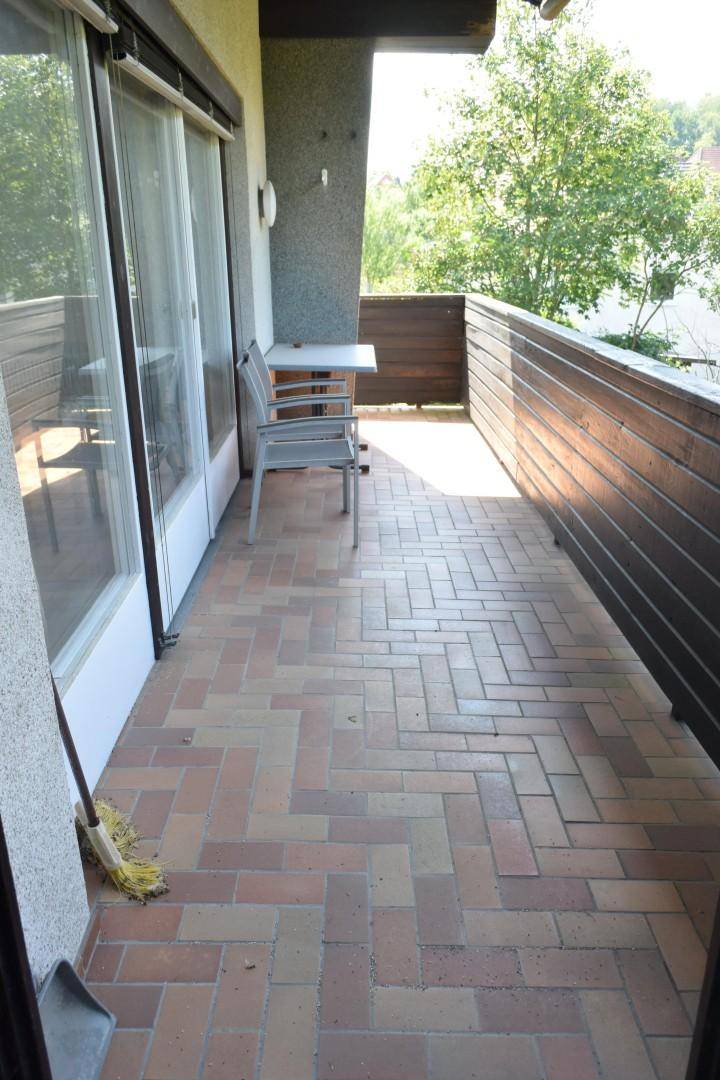 Geräumiger Balkon mit Ziegelboden und Holzbalkonbrüstung, möbliert mit einem kleinen Tisch und Stühlen.