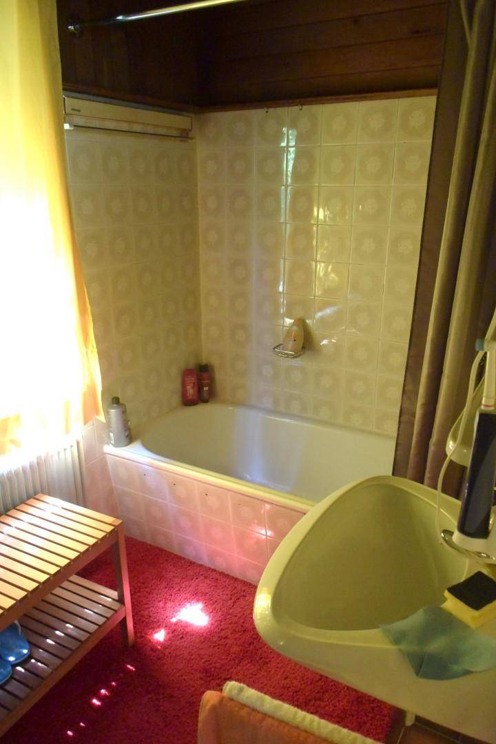 Badezimmer im Stil der 80er Jahre mit Badewanne, gemusterten Fliesen und rotem Teppichboden.