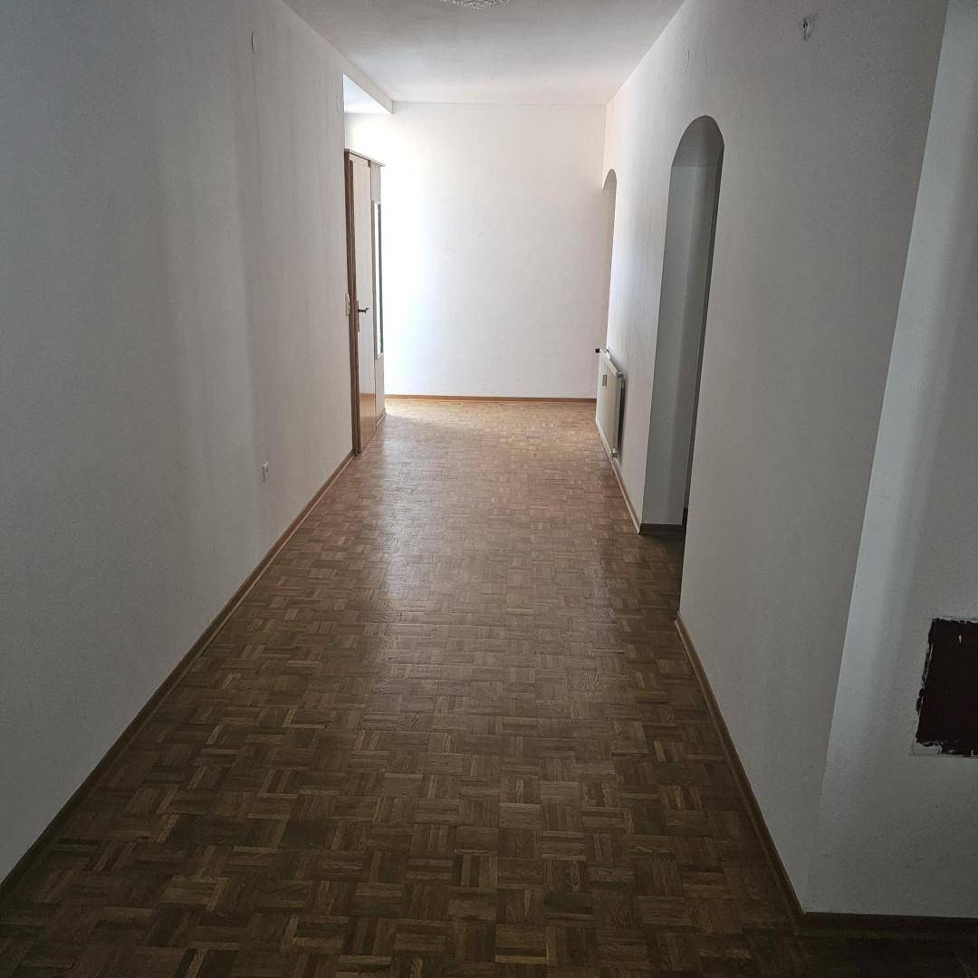 Heller Flur mit Parkettboden und weißen Wänden, der zu weiteren Räumen führt.