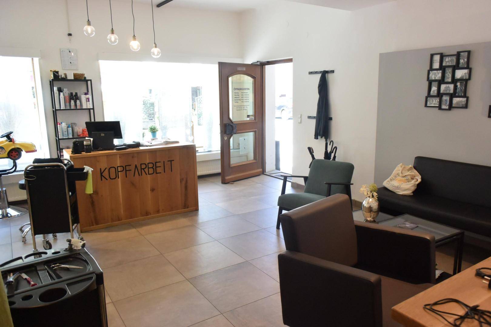 Heller Empfangsbereich eines Salons mit Holztresen und Sitzgelegenheiten.