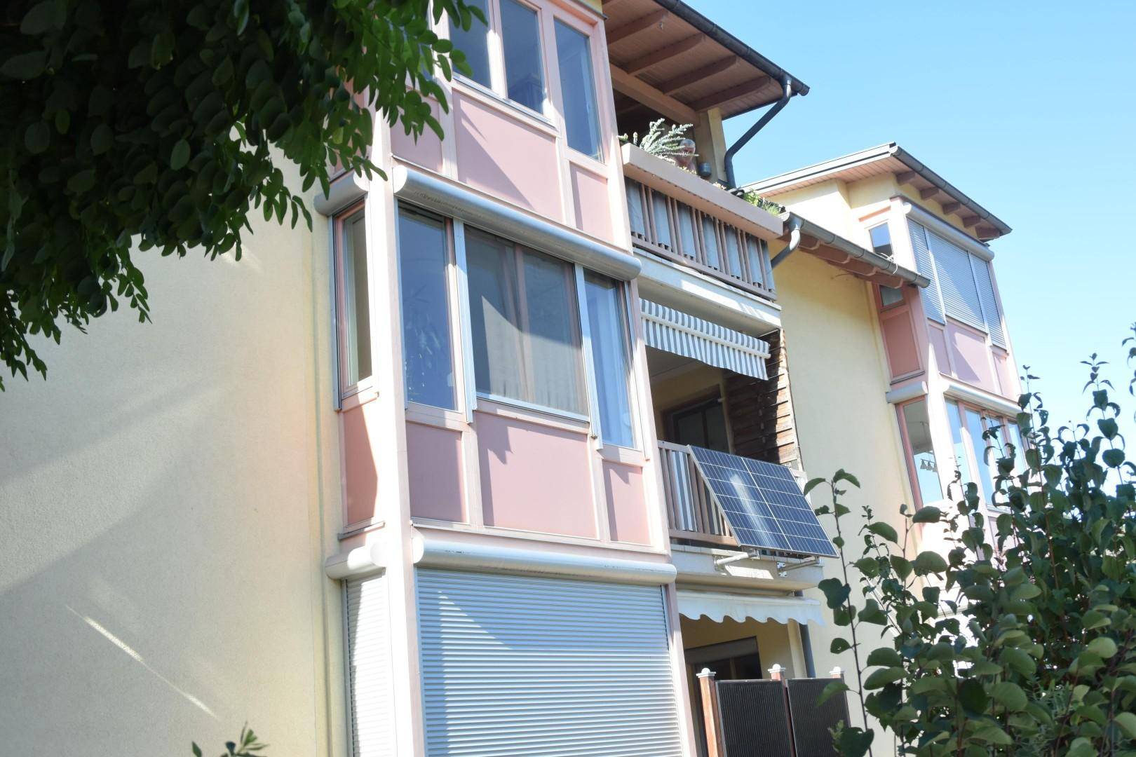 Fassade eines Mehrfamilienhauses mit Balkonen, Rollläden und Solarpaneelen.