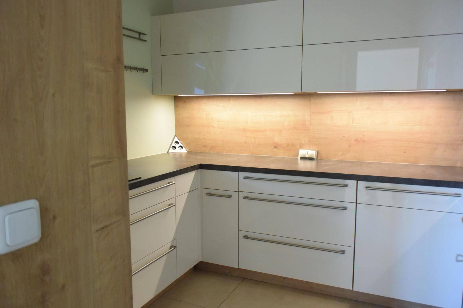 Moderne Küche mit weißen Hochglanzfronten, Holzrückwand und integrierter Beleuchtung.