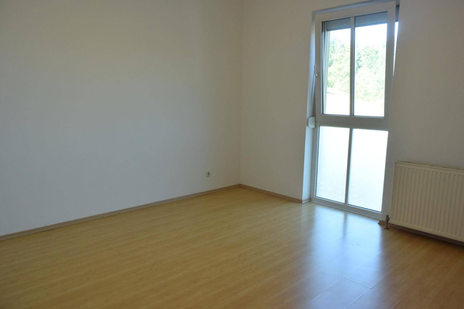 Leeres Schlafzimmer mit Laminatboden und Zugang zu einem Balkon.