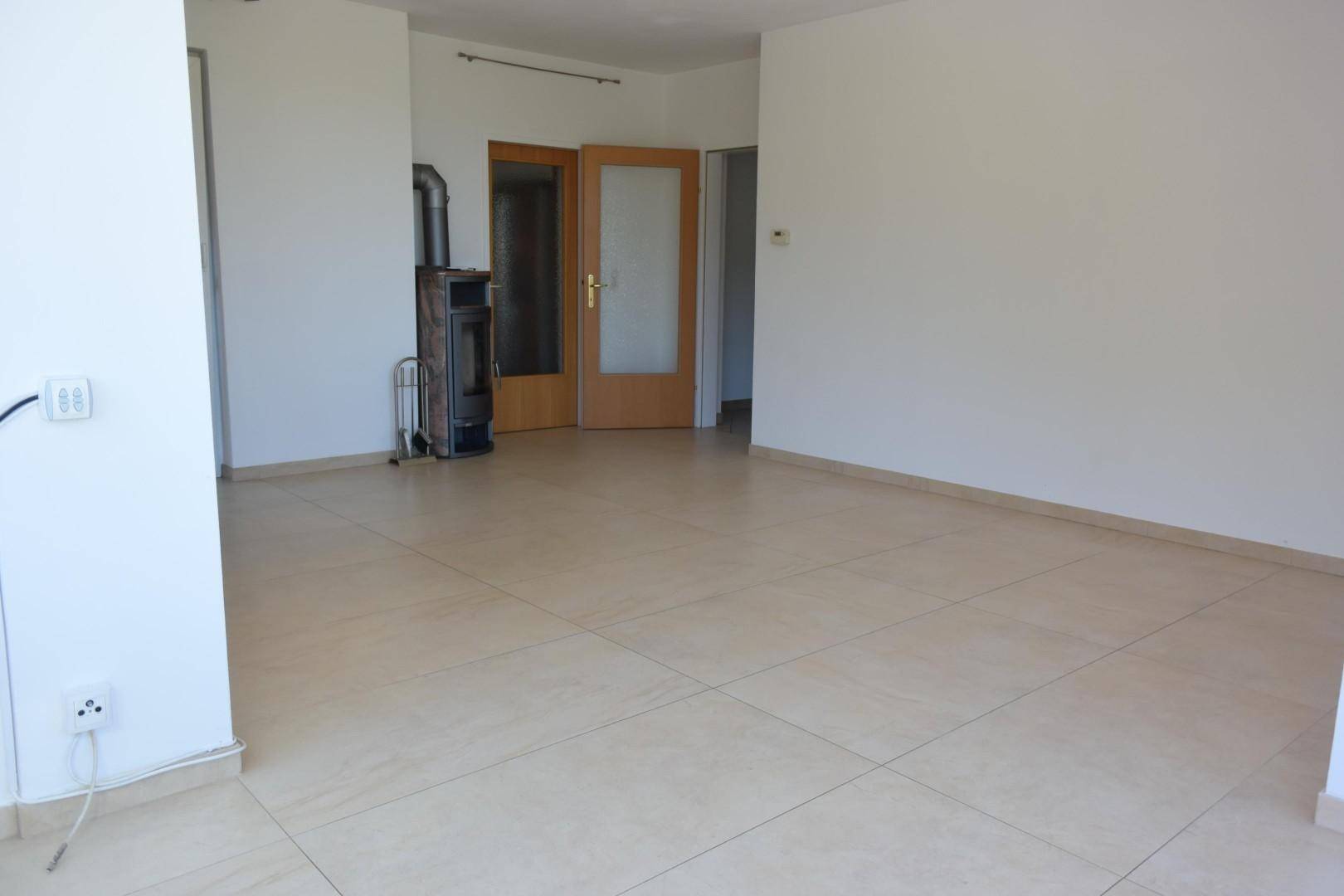 Leeres Wohnzimmer mit Fliesenboden und einem modernen Holzofen als Heizquelle.