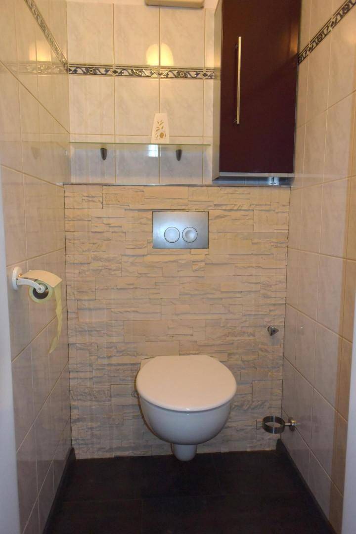 Gäste-WC mit Wand-WC und dekorativer Steinwandverkleidung.