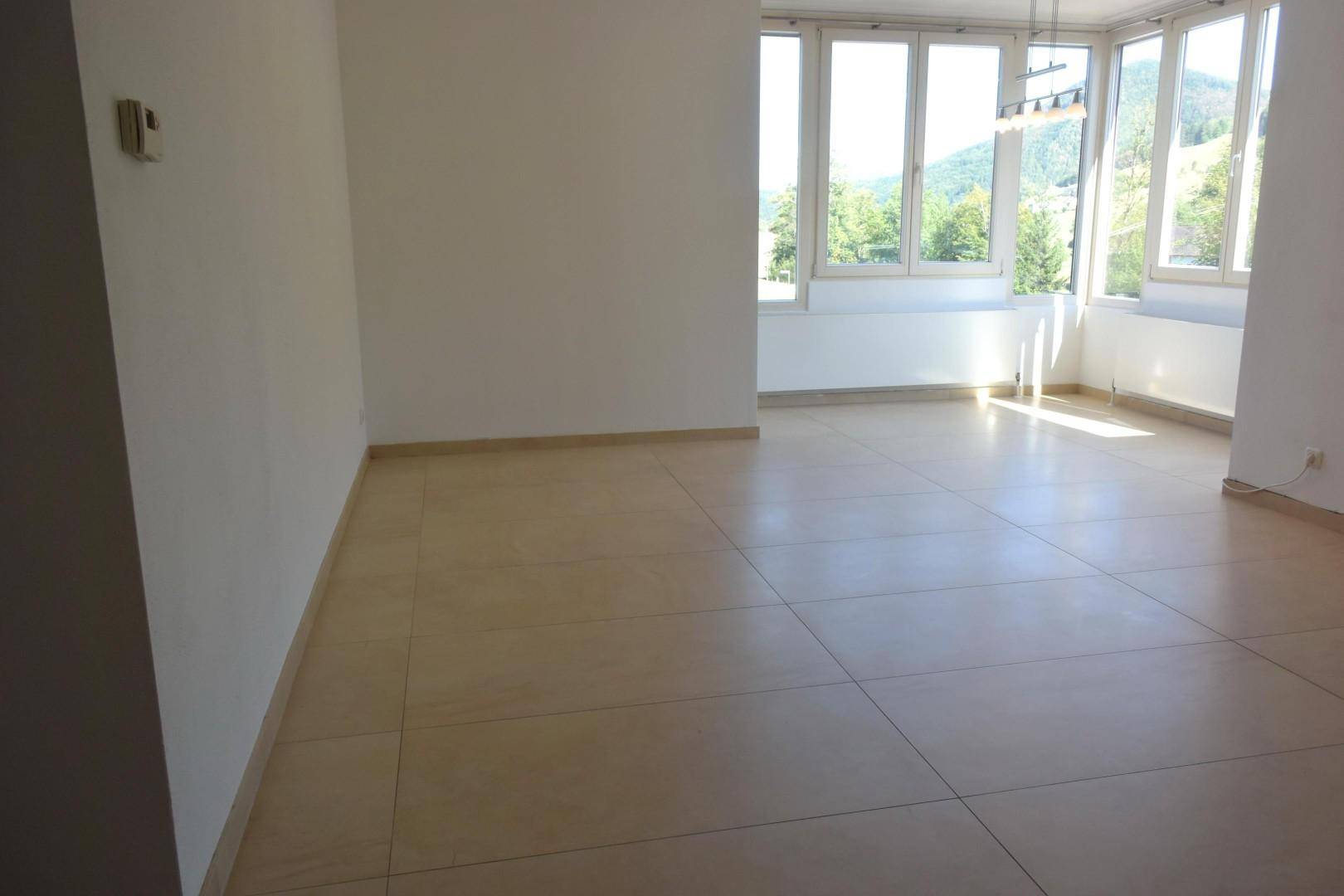 Geräumiges, helles Zimmer mit Fliesenboden und weitem Blick auf die grüne Landschaft.