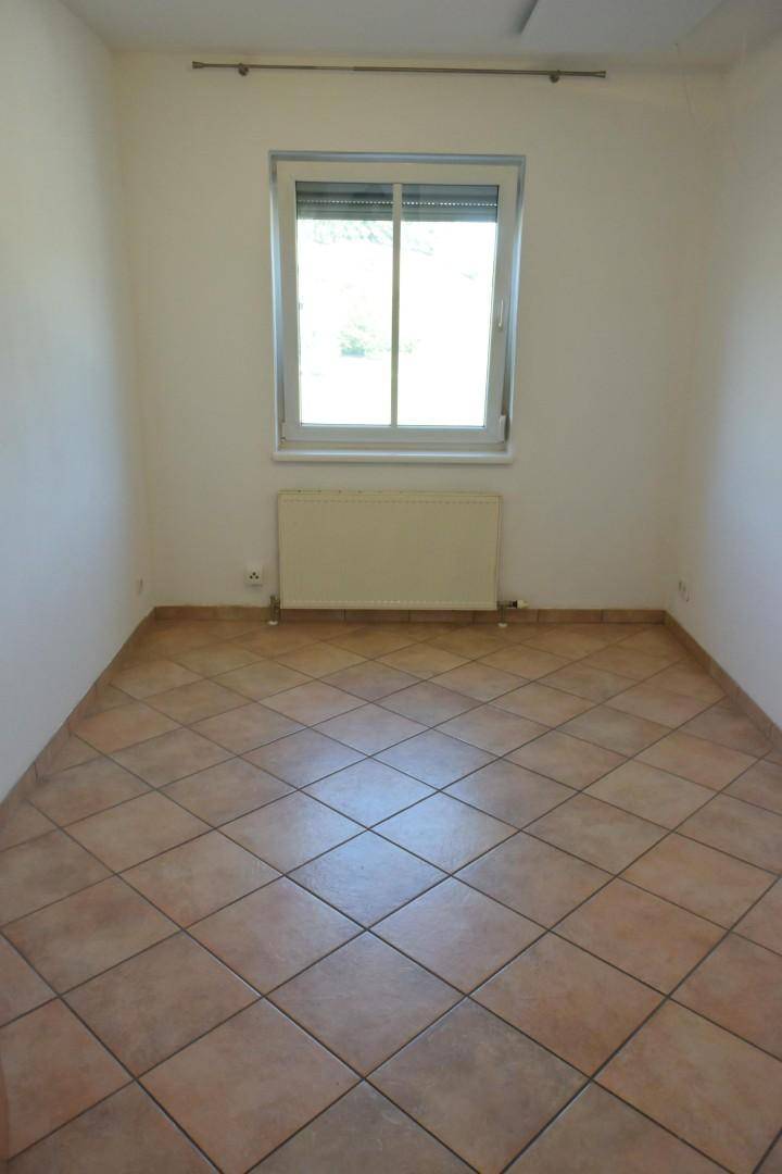 Leeres Zimmer mit diagonal verlegten Fliesen, Fenster und Heizkörper.