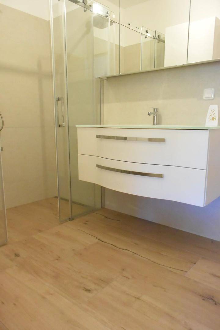 Modernes Badezimmer mit schwebendem Waschtisch, Spiegelschrank und Glasdusche.