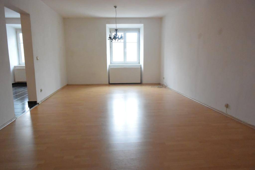 Geräumiges, leeres Wohnzimmer mit hellem Laminatboden und einem Fenster.