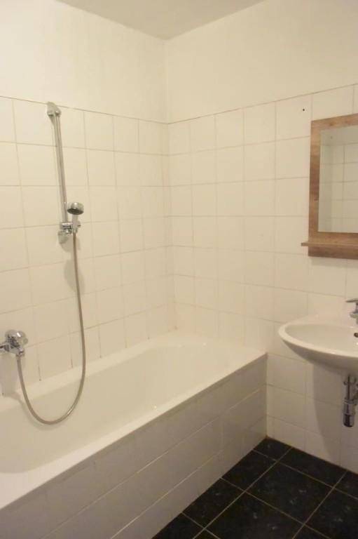 Helles Badezimmer mit Badewanne, Dusche und Waschbecken, ausgestattet mit weißen Fliesen.
