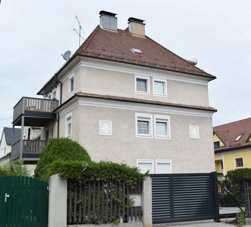 Wohngebäude mit traditionellem Satteldach, Balkonen und einer gepflegten Hecke vor dem Grundstück.