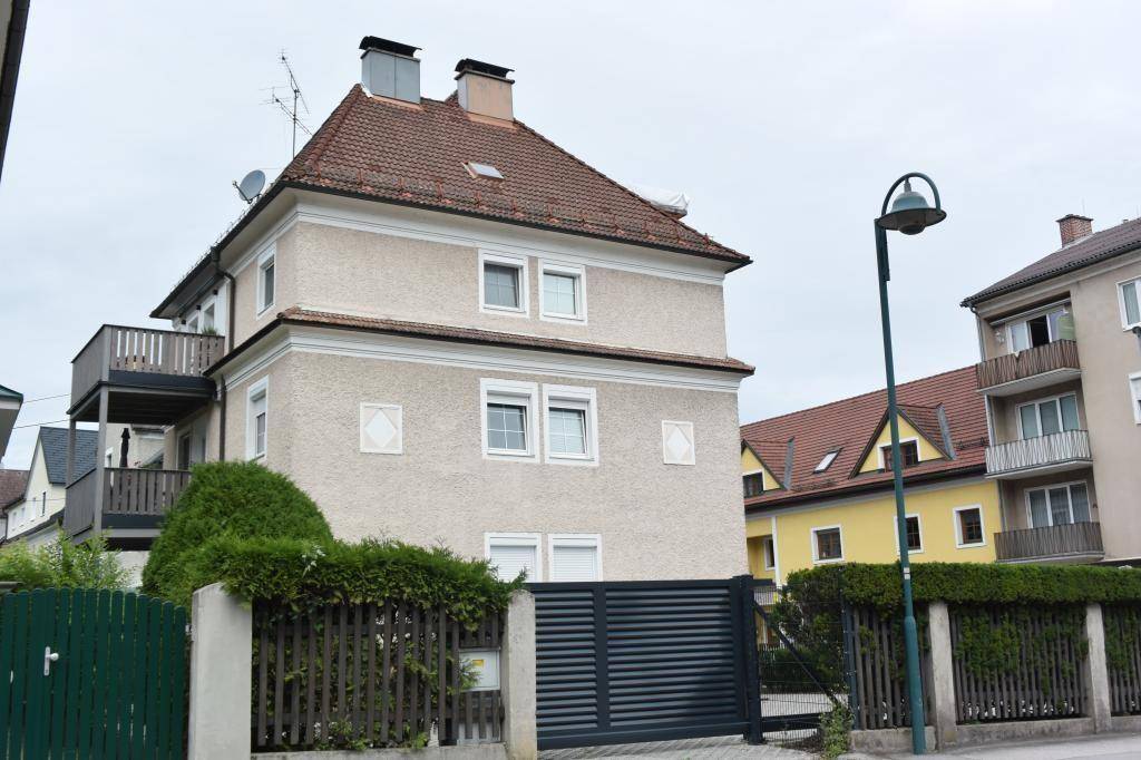 Ansicht eines Wohnhauses mit Balkonen, Satteldach und einem modernen Zaun im Vordergrund.