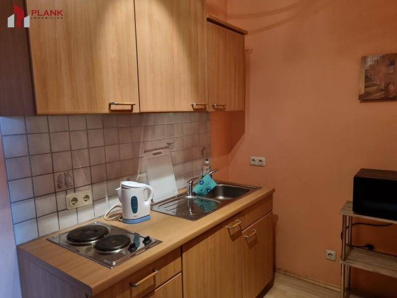 Kleine Küchenzeile mit Kochplatten, Spüle und Holzschränken, ideal für eine Ferienwohnung.