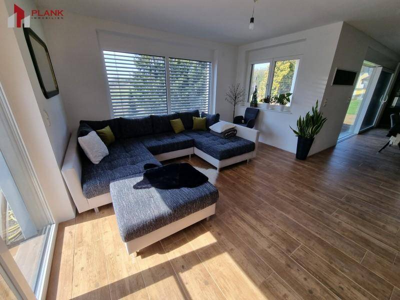Helles Wohnzimmer mit großem Ecksofa, Holzboden und Zugang zum Garten.
