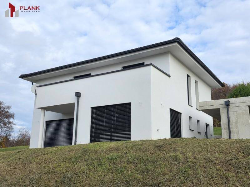 Modernes Einfamilienhaus mit weißer Fassade, dunklen Fensterläden und Balkon.