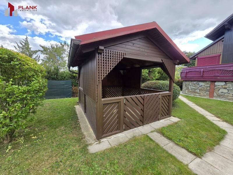Gartenbereich mit einem hölzernen Pavillon, umgeben von Rasen und Hecken.