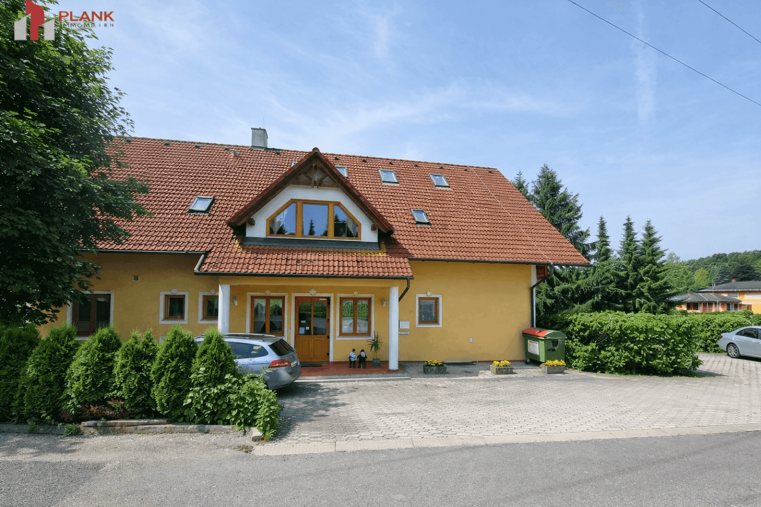 Traditionelles Haus mit gelber Fassade, rotem Ziegeldach und großem Vorplatz mit Parkmöglichkeiten.