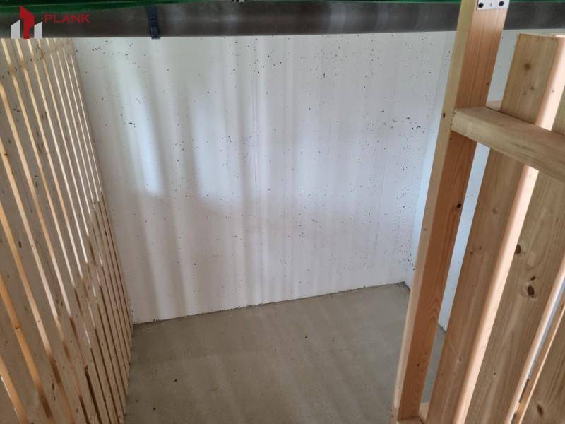 Einfacher Abstellraum mit Betonboden und Holzlattenwänden für Lagerzwecke.