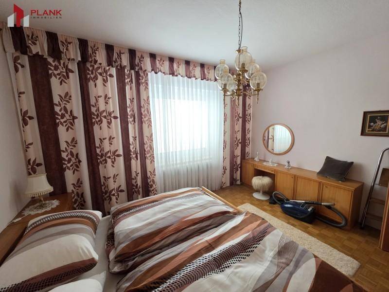 Schlafzimmer mit Holzparkett, großem Fenster und traditionellem Kronleuchter.