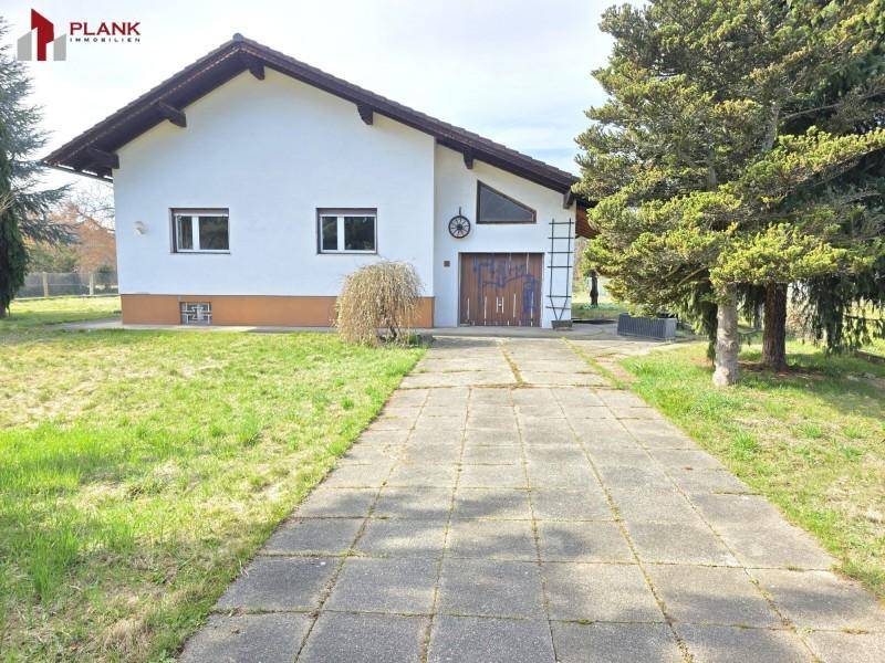 Ansicht des Hauses mit gepflasterter Auffahrt und integrierter Garage, umgeben von Grünflächen.