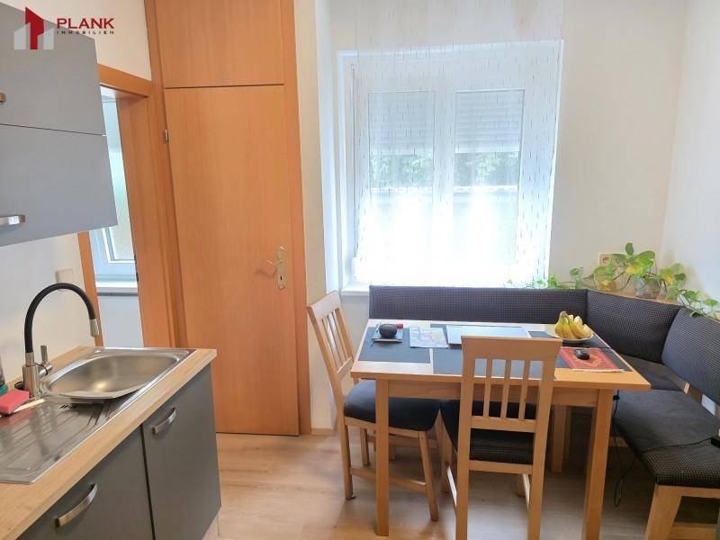 Kleine Küche mit Spüle, grauen Unterschränken und integriertem Essbereich am Fenster.