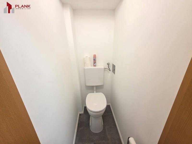 Kleines separates WC mit weißer Toilette und dunklen Bodenfliesen.