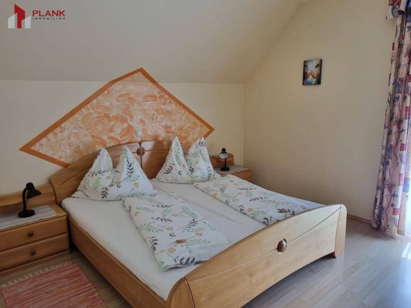 Helles Schlafzimmer im Dachgeschoss mit Doppelbett, Holzmöbeln und schrägen Decken.