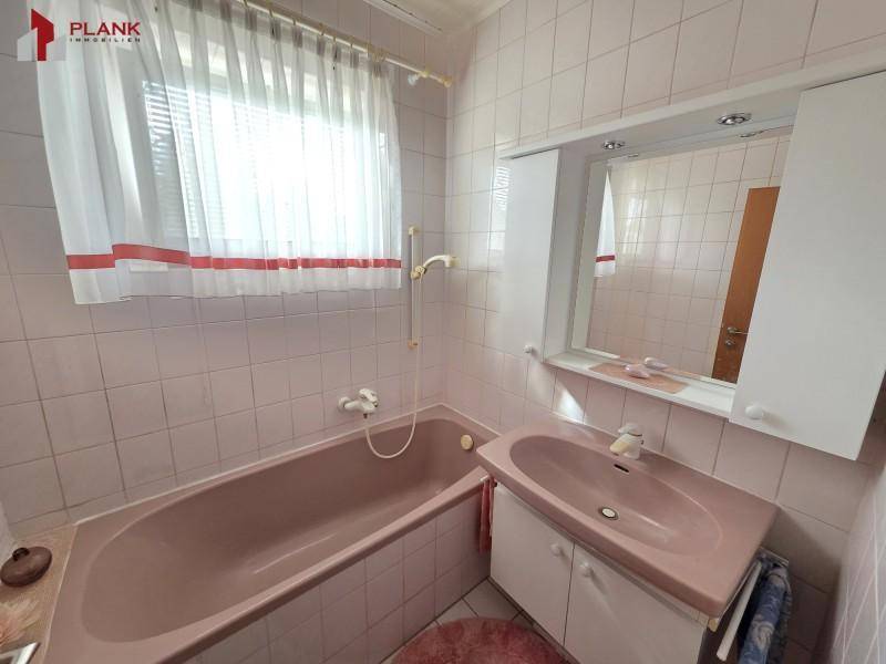 Badezimmer im 80er-Jahre-Stil mit rosa Fliesen, Badewanne und Einzelwaschbecken.