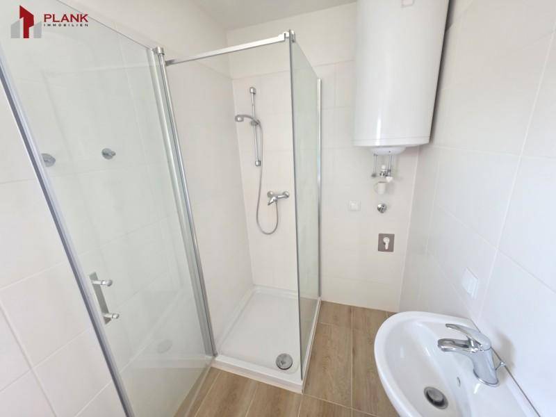 Modernes Badezimmer mit Duschkabine, Waschbecken und Warmwasserboiler.