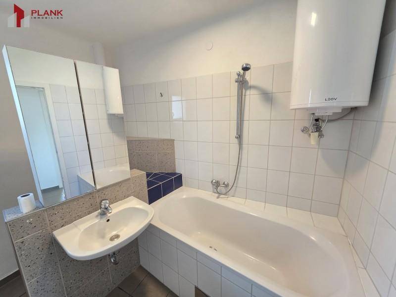 Badezimmer mit Badewanne, Duscharmatur, Waschbecken und einem Spiegelschrank über dem Waschtisch.