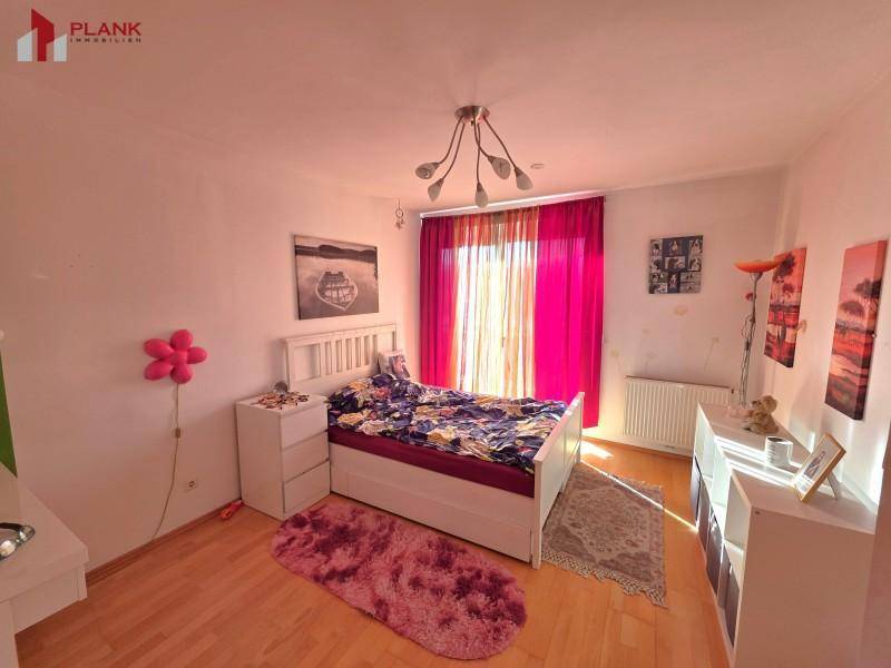 Helles Schlafzimmer mit Holzboden, Doppelbett und farbenfroher Dekoration.