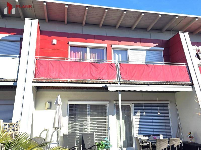 Moderne Reihenhausfassade mit roten Paneelen, Balkonen und einer Terrasse.