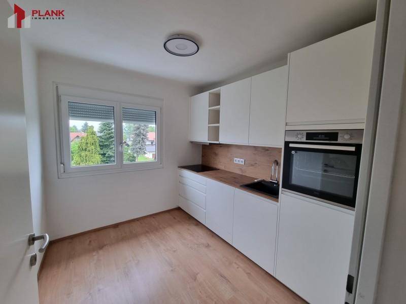 Funktionale Küche mit weißen Schränken, integriertem Backofen und Fenster mit Rollläden.