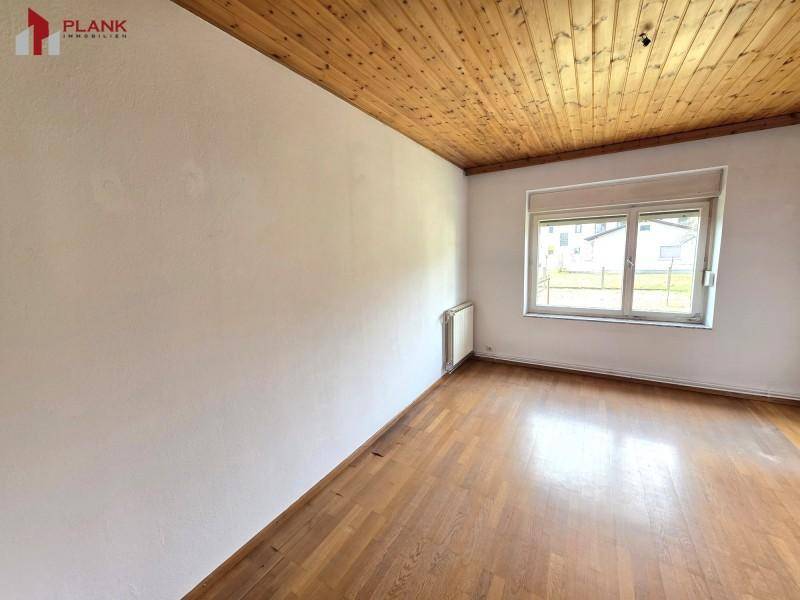 Ruhiges Schlafzimmer mit Holzdeckenverkleidung und Parkettboden, mit Blick ins Grüne.