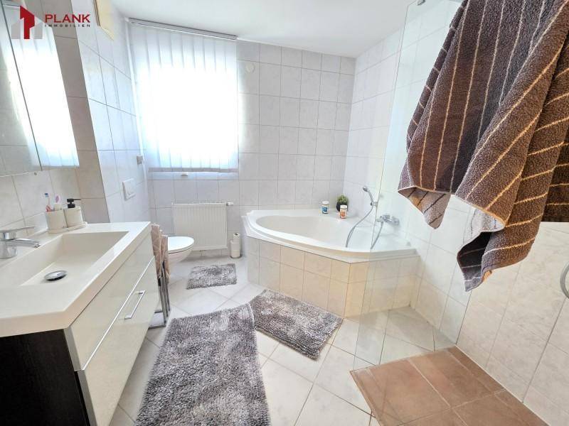 Helles Badezimmer mit Eckbadewanne, modernem Waschbecken und Fenster.
