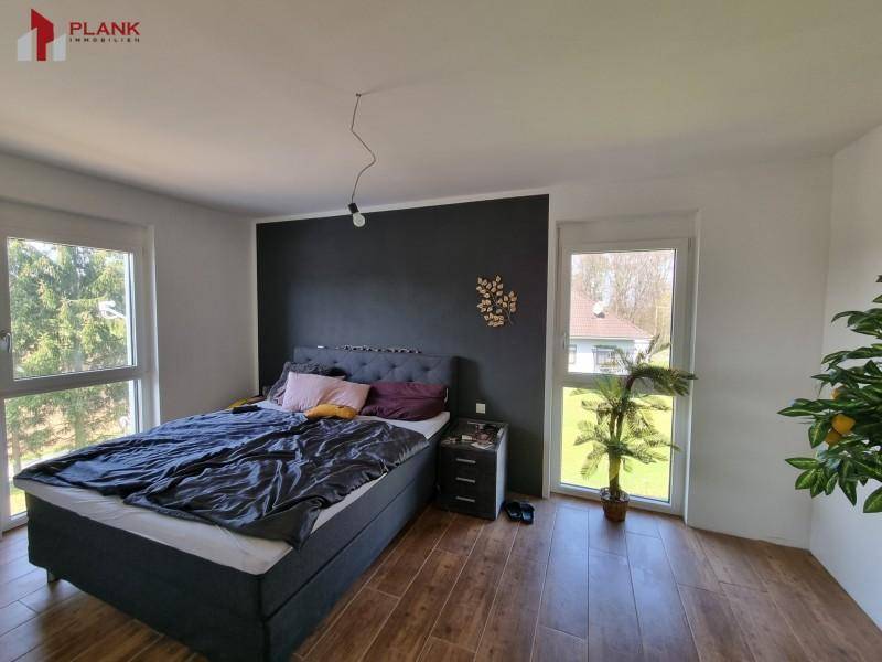 Helles Schlafzimmer mit Doppelbett, dunkler Wand und Blick ins Grüne.