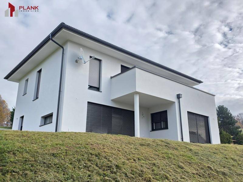 Modernes Einfamilienhaus auf einem Hügel mit weißer Fassade und dunklen Fensterläden.