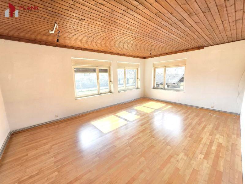 Helles Wohnzimmer mit Holzdeckenverkleidung und Parkettboden, durchflutet von natürlichem Licht.