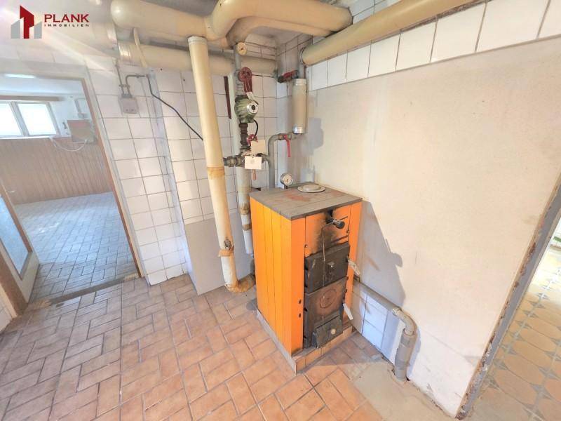 Heizraum mit einem älteren Festbrennstoffkessel und Fliesenboden, funktional und geräumig.