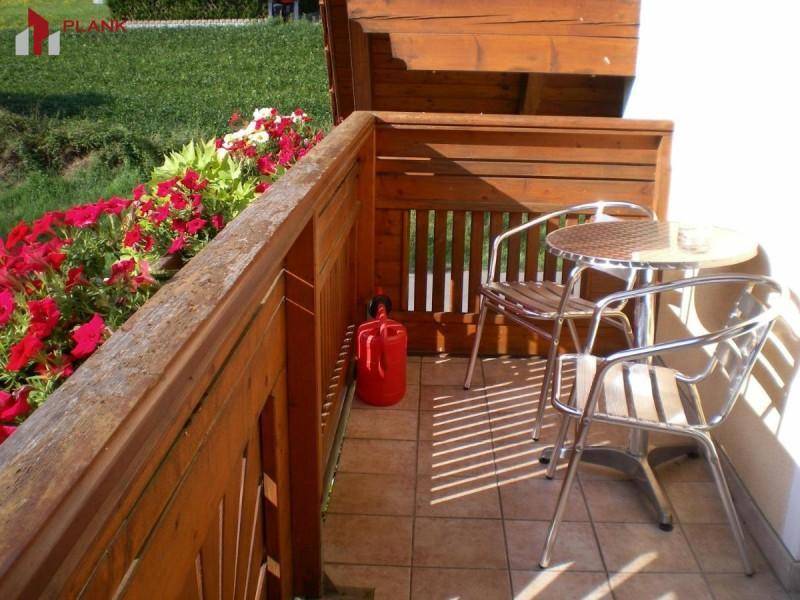 Kleiner Balkon mit Holzboden, Sitzgelegenheiten und bunten Blumenkästen.
