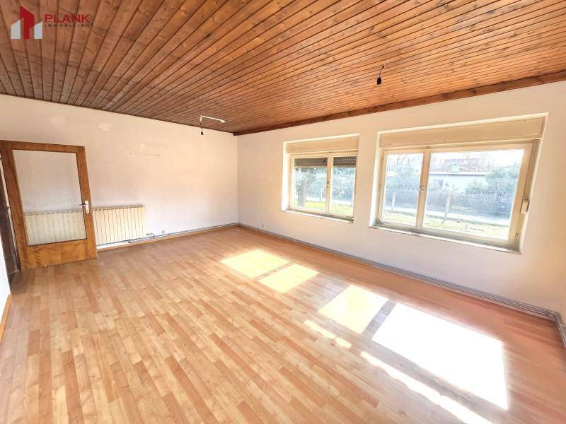 Helles Wohnzimmer mit Holzdeckenverkleidung und Parkettboden, durchflutet von natürlichem Licht.