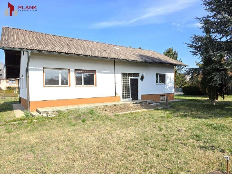 Rückseite des Hauses mit großem Gartenbereich und Zugangstür, umgeben von viel Grün.
