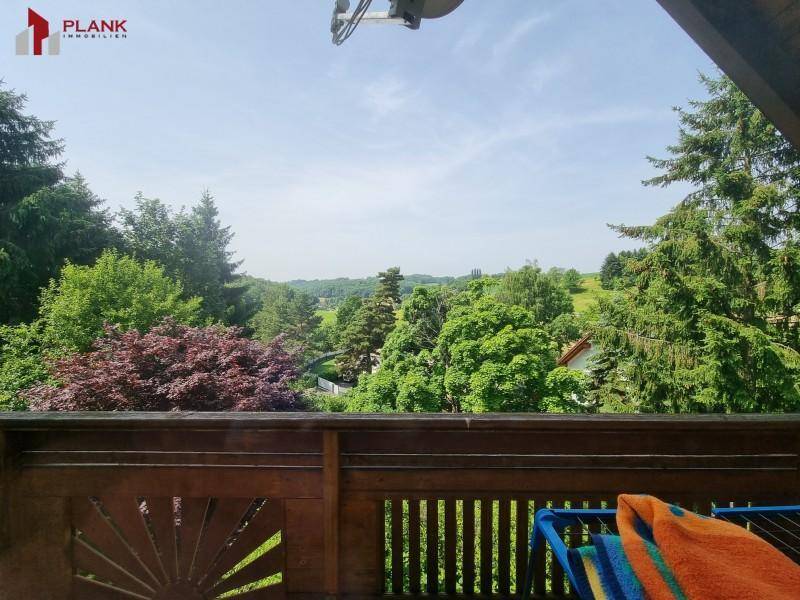 Balkon mit Holzbalken und weitem Blick über die grüne Landschaft und Bäume.