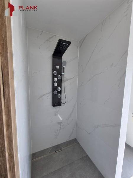 Geräumige begehbare Dusche mit modernen Fliesen und schwarzer Duschsäule.